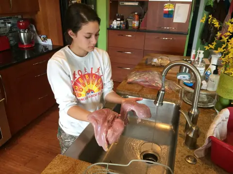 Une jeune femme dans une cuisine tient de la viande d'un dindon sauvage au-dessus d'un évier