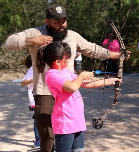 Le Ranger Garza entraîne une fille sur la bonne forme tout en tirant un arc.