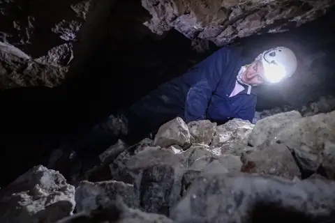 Des biologistes rampant sur le côté pour traverser un passage étroit entre un sol en pierre et un plafond en pierre dans une mine