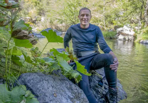 un homme assis sur un rocher à côté d'une rivière posant pour la caméra