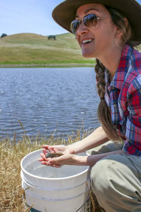 Une femme s'accroupit tout en tenant une salamandre dans ses mains