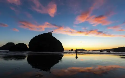 un coucher de soleil coloré sur l'océan avec un homme marchant au loin.