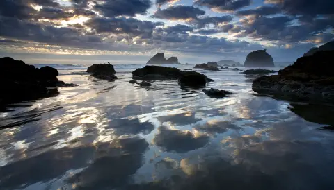 un coucher de soleil nuageux sur l'océan avec le ciel se reflétant dans l'eau.
