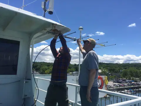 Image de deux hommes installant une antenne de suivi sur un bateau
