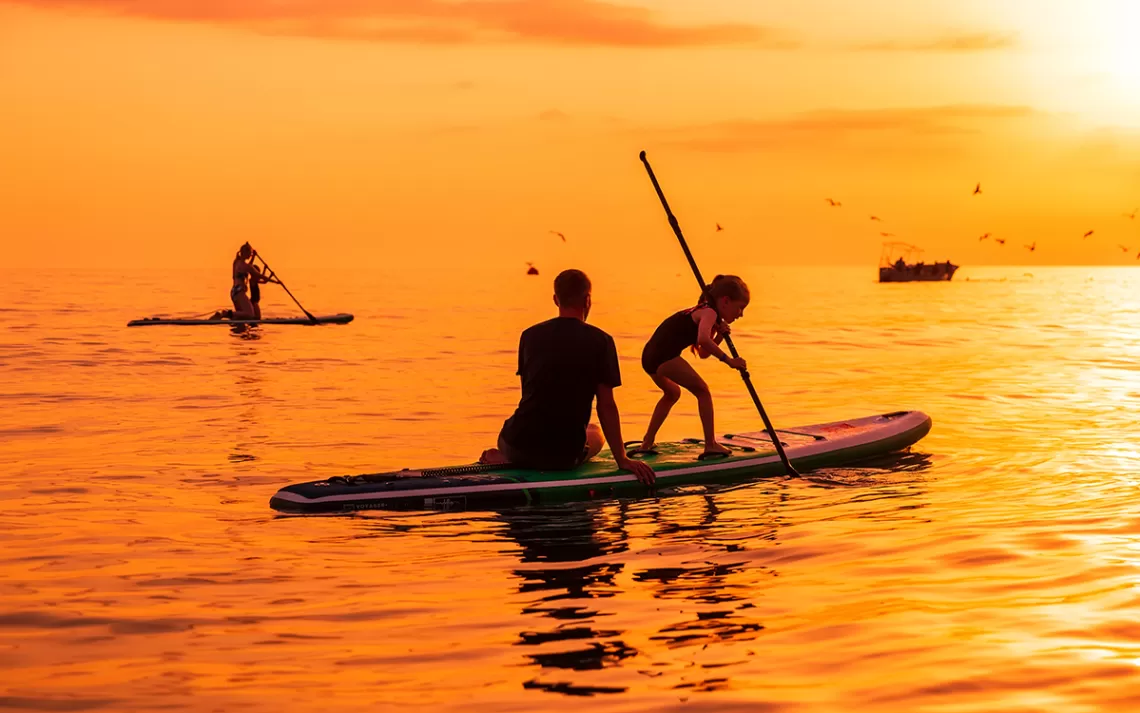 Paddleboarders silhouetté contre un ciel orange et la mer. 