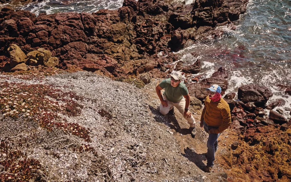 Brian Holguin et un autre homme se tiennent sur une falaise rocheuse avec l'océan derrière eux.
