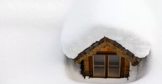 toit enneigé avec une petite fenêtre qui sort de la couverture de neige