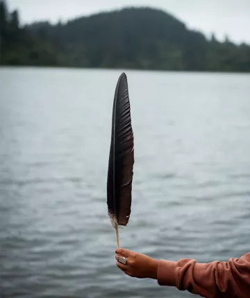 Plume de Condor tenue par une main portant une bague en argent avec un lac en arrière-plan