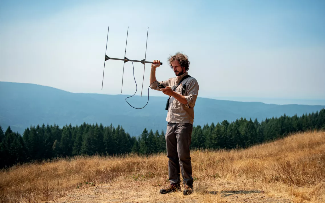 Patrick Myers se tient dans un champ herbeux sec au sommet d'une montagne et tient un appareil de télémétrie devant lui.