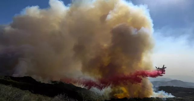 Nuage de retardateur de feu éclatant sur un paysage vallonné vert-brun en feu, sur un ciel bleu.