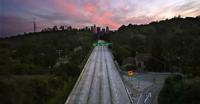 Une autoroute vide entourée de verdure vue du ciel, atteignant un coucher de soleil rose violet.