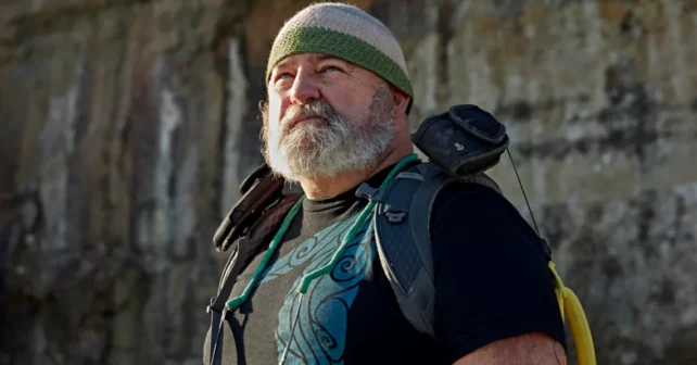 Wayne Thompson, qui a une barbe grise et porte un bonnet et un sac à dos, regarde au loin.