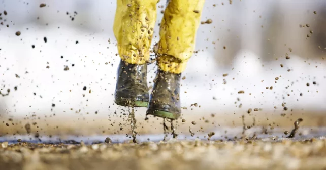 Enfant photographié à partir de la taille, sautant dans une flaque d'eau avec des bottes de pluie jaunes