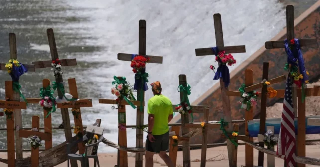 Un homme passe devant les croisements et les fleurs qui forment un mémorial de fortune le long de la rivière Guadalupe alors que les comités Sénat et House Select sur la préparation aux catastrophes et les inondations tiennent une audience publique à Kerrville, au Texas,