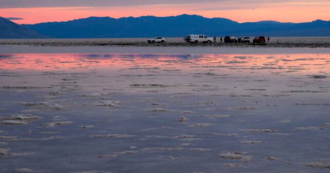 Vehículos en una llanura salina al atardecer con reflejos en el agua, imagen asociada al aumento de temperaturas globales