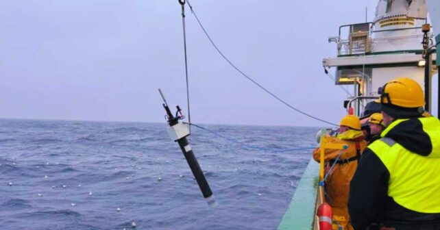 Equipo en un barco desplegando un instrumento oceanográfico de medición en el mar con grúa y cable.