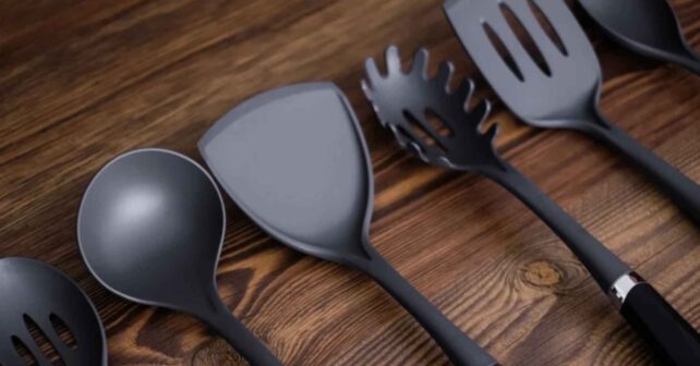 Utensilios de cocina negros de plástico sobre mesa de madera (espátula, cucharón y pala ranurada)