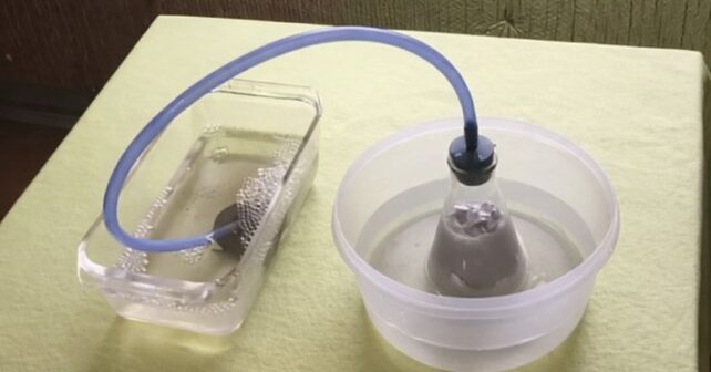 Experimento de producción de hidrógeno a partir de agua mediante reacción química en laboratorio con sistema de tubos y burbujas.